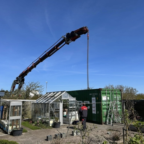 Krankørsel med container i haveområde ved drivhuse i Aalborg.