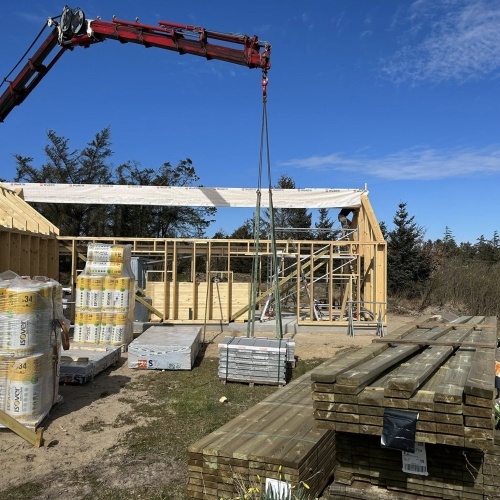 Krankørsel med træbjælke løftet på plads mellem husets vægge.