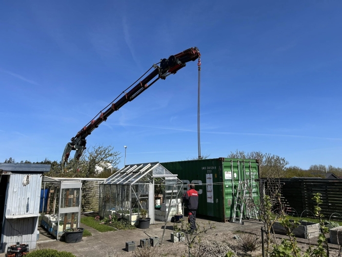 Krankørsel med container i haveområde ved drivhuse i Aalborg.