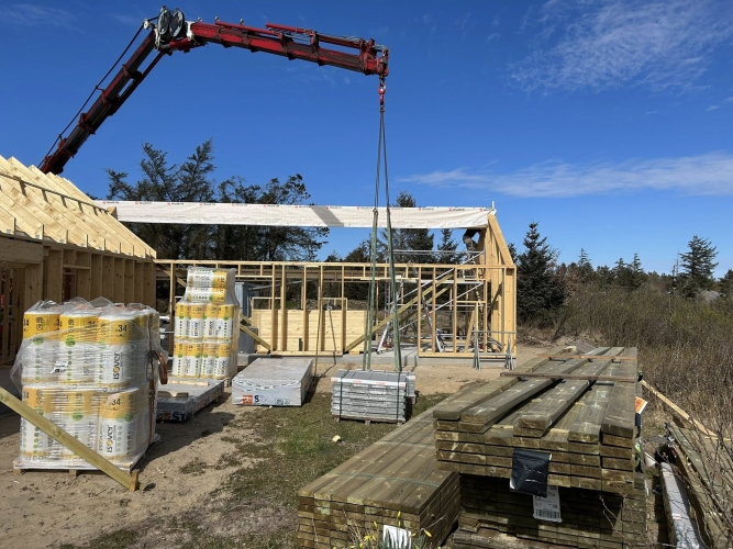 Krankørsel med træbjælke løftet på plads mellem husets vægge.